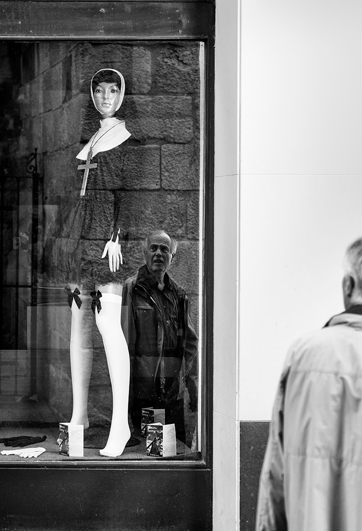 Un maniquí en un escaparate y un reflejo de personas.